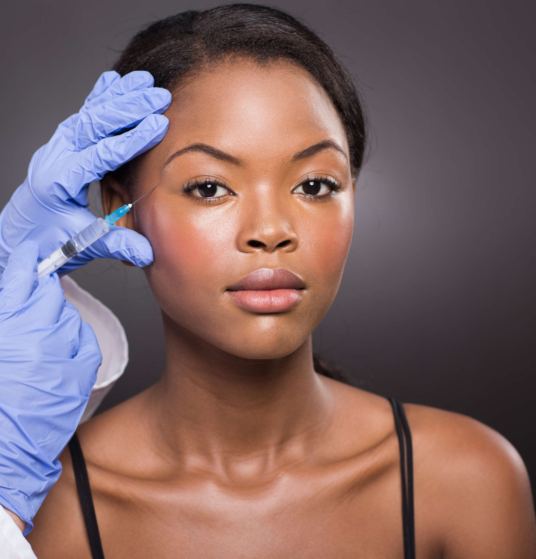 cosmetic surgeon injecting african american girl face on black background